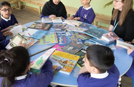 many pupils sit round a circular table with a teacher reading